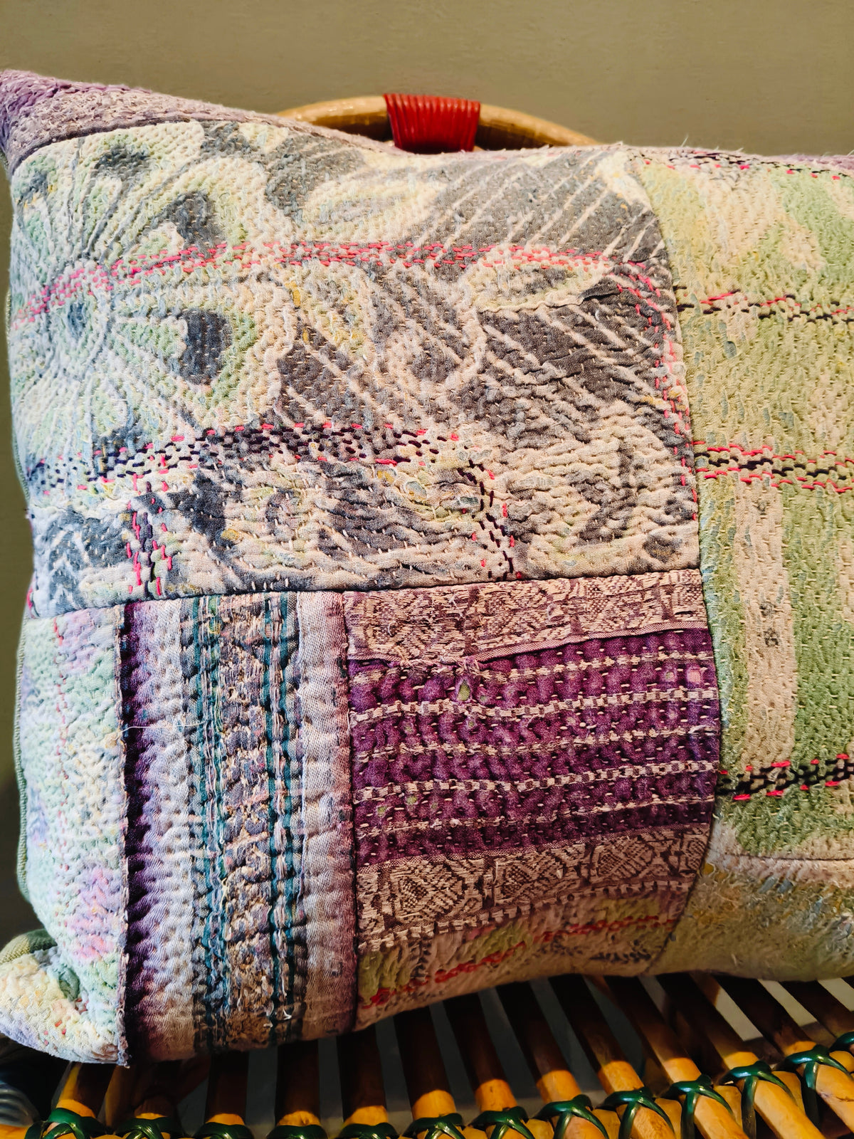 A square patchwork quilted square cushion made from vintage kantha quilts. Muted purple, green, grey, and beige tones. 100% duck down inner. 